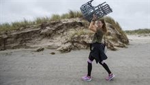Meisje draagt een stoel boven haar hoofd op het strand